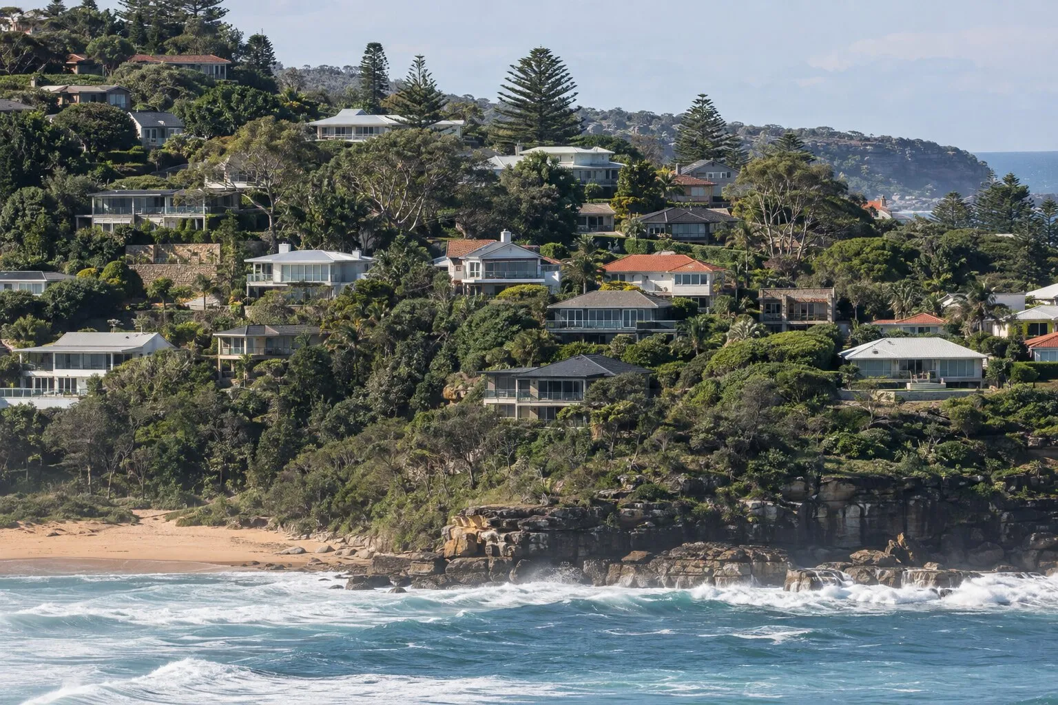 Coastal roofing, Northern Beaches: hillside of tile and Colorbond roofs stepping down to a surf beach