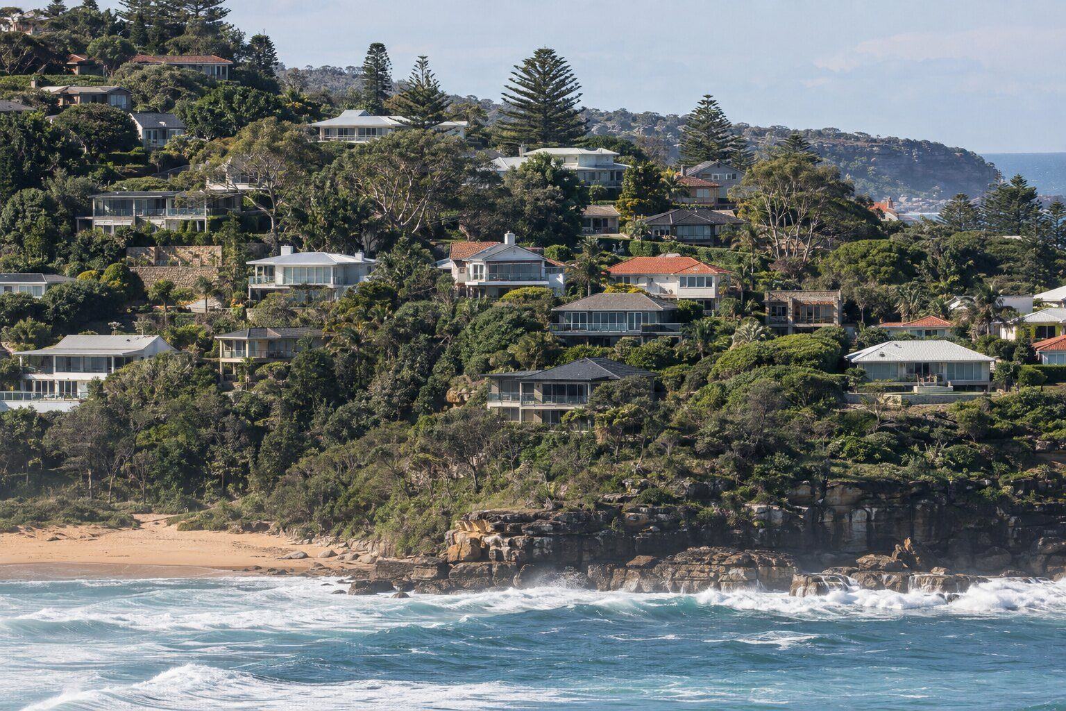 Roofing guides, Northern Beaches: hillside of tile and Colorbond roofs stepping down to a surf beach