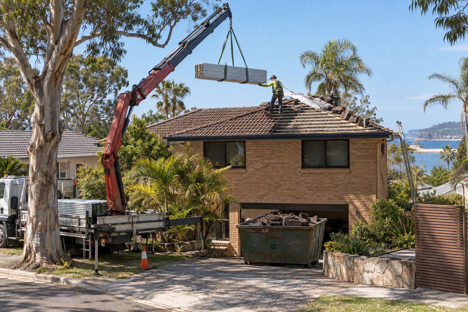 Roof replacement cost, Northern Beaches: crane truck lifting bundled steel roof sheets onto a two-storey brick home, with the old roof tiles in a skip bin