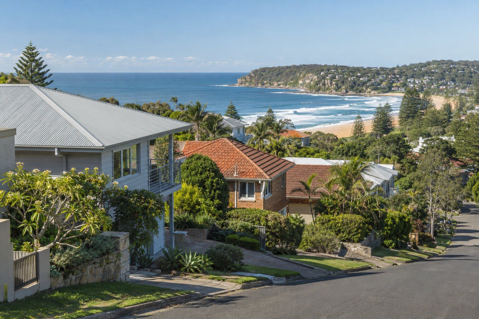 Roofing, Freshwater: hillside weatherboard and brick homes with Colorbond and terracotta roofs above a surf beach